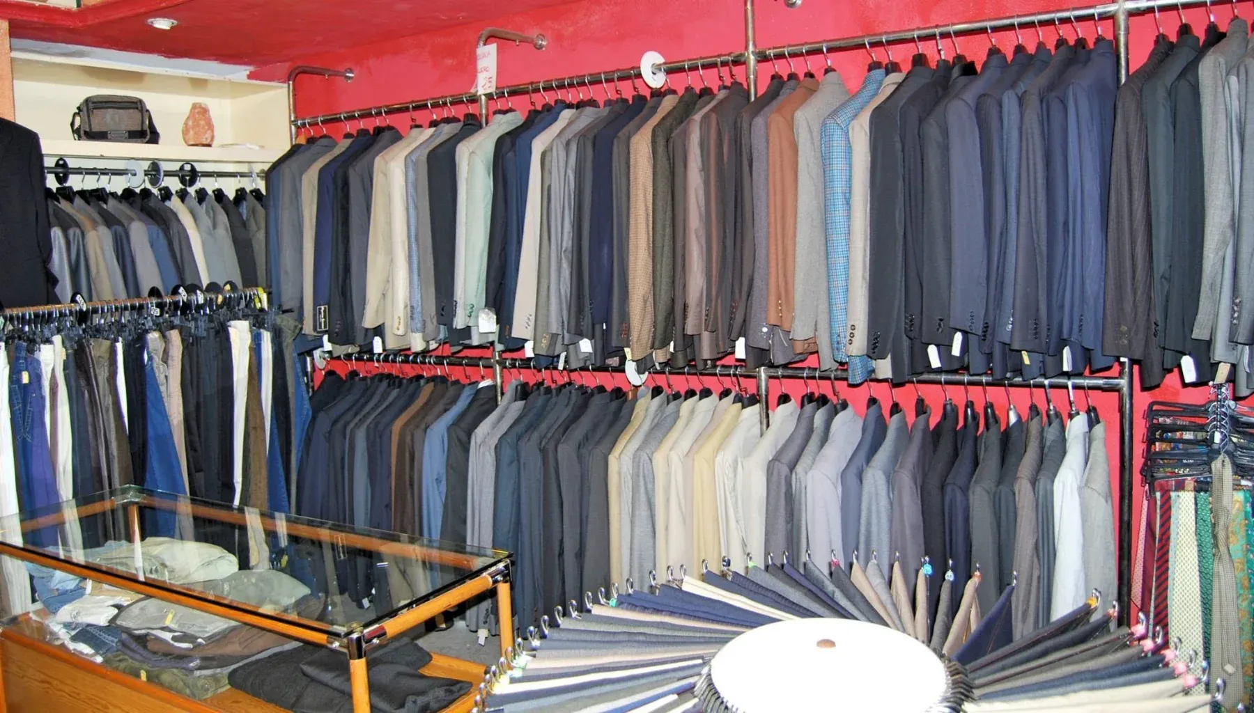 Interior de Mirezandis: filas de americanas y trajes colgados sobre la pared roja