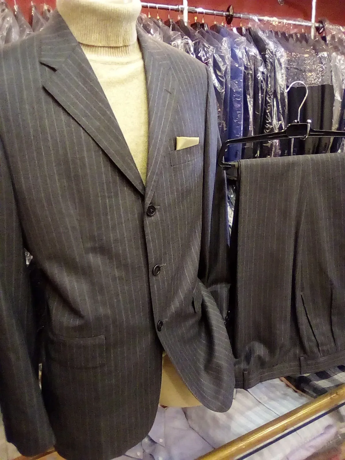 Traje gris a raya diplomática en maniquí, con el perchero de trajes enfundados detrás